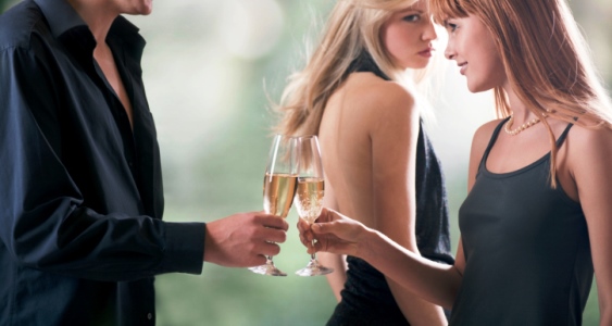 Young couple holding glasses with champagne and woman looking for them, outdoors, focus on woman with red hair and man